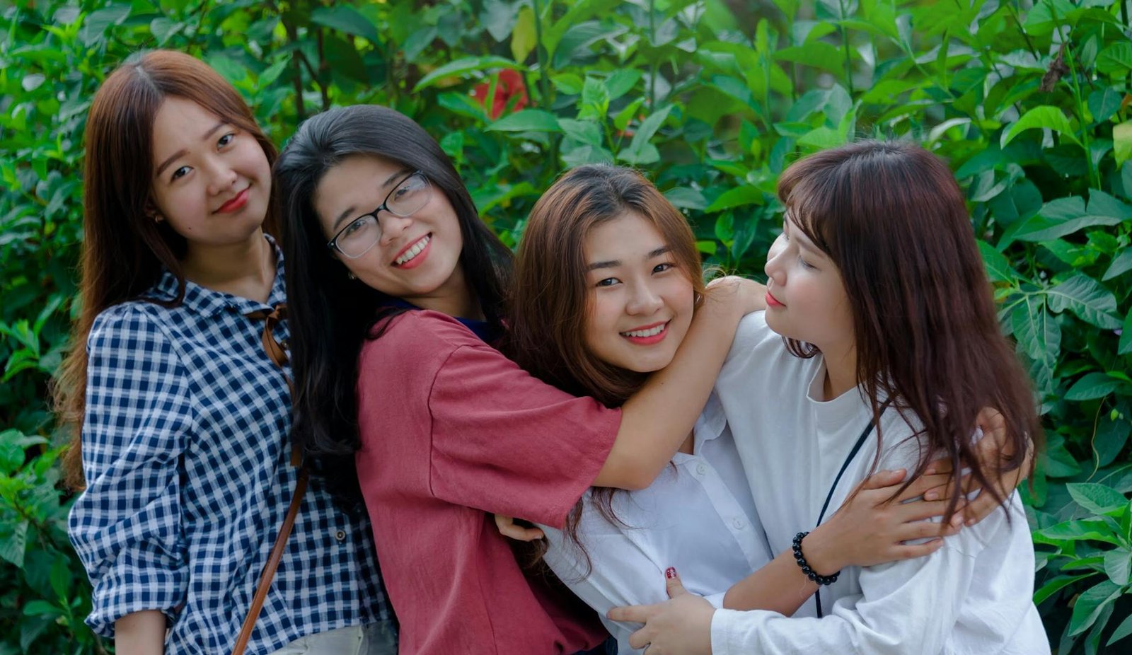 Four young women smiling and embracing outdoors, conveying friendship and happiness.