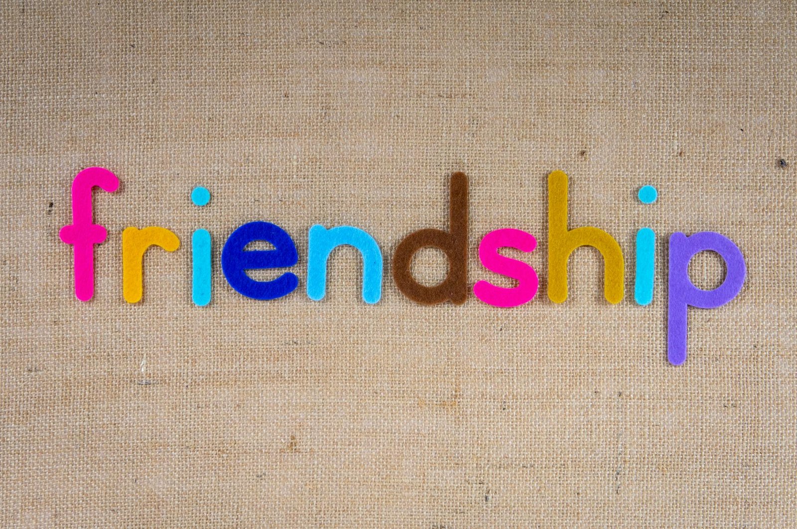 Vibrant letters spelling 'friendship' on a textured brown burlap background.