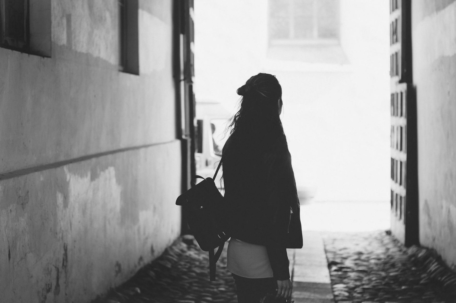 Silhouette of a woman walking in a cobblestone alley. Moody and introspective.