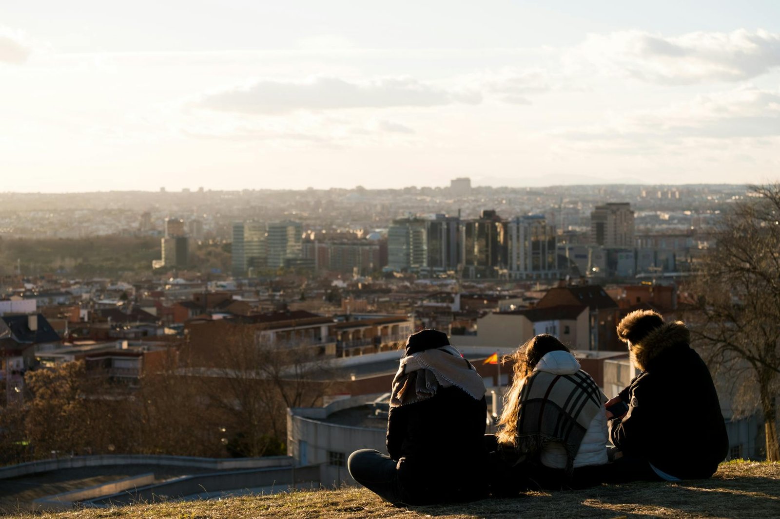 Three people sitting on a hill enjoying the view of Madrid's skyline at sunset.