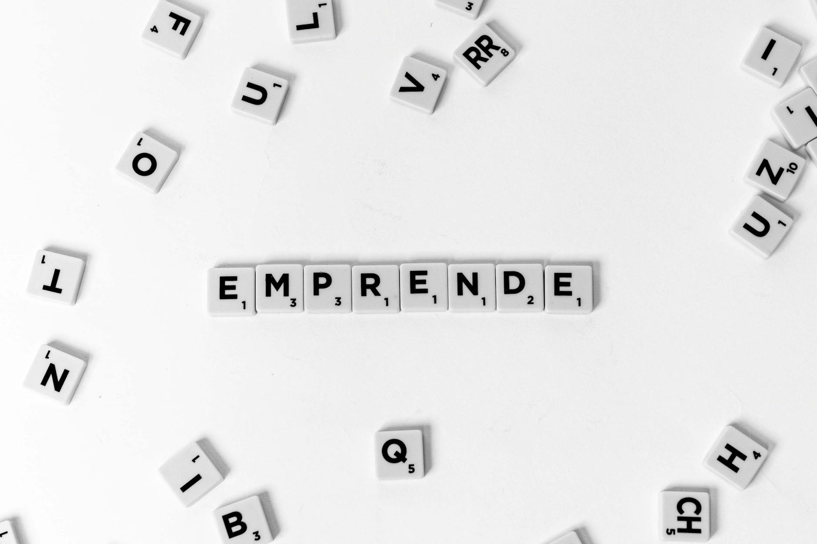 Scrabble tiles laid out to spell 'EMPRENDE' creatively on white background.