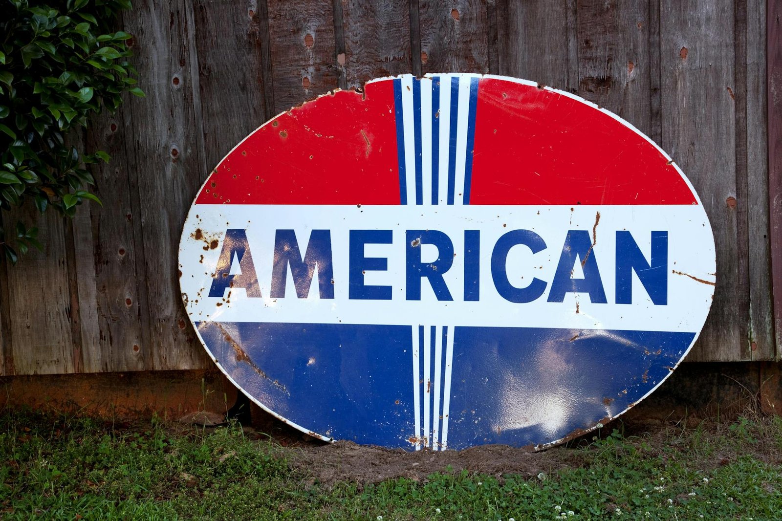 Antique oval American sign with rust spots against a wooden fence, emphasizing vintage Americana charm.