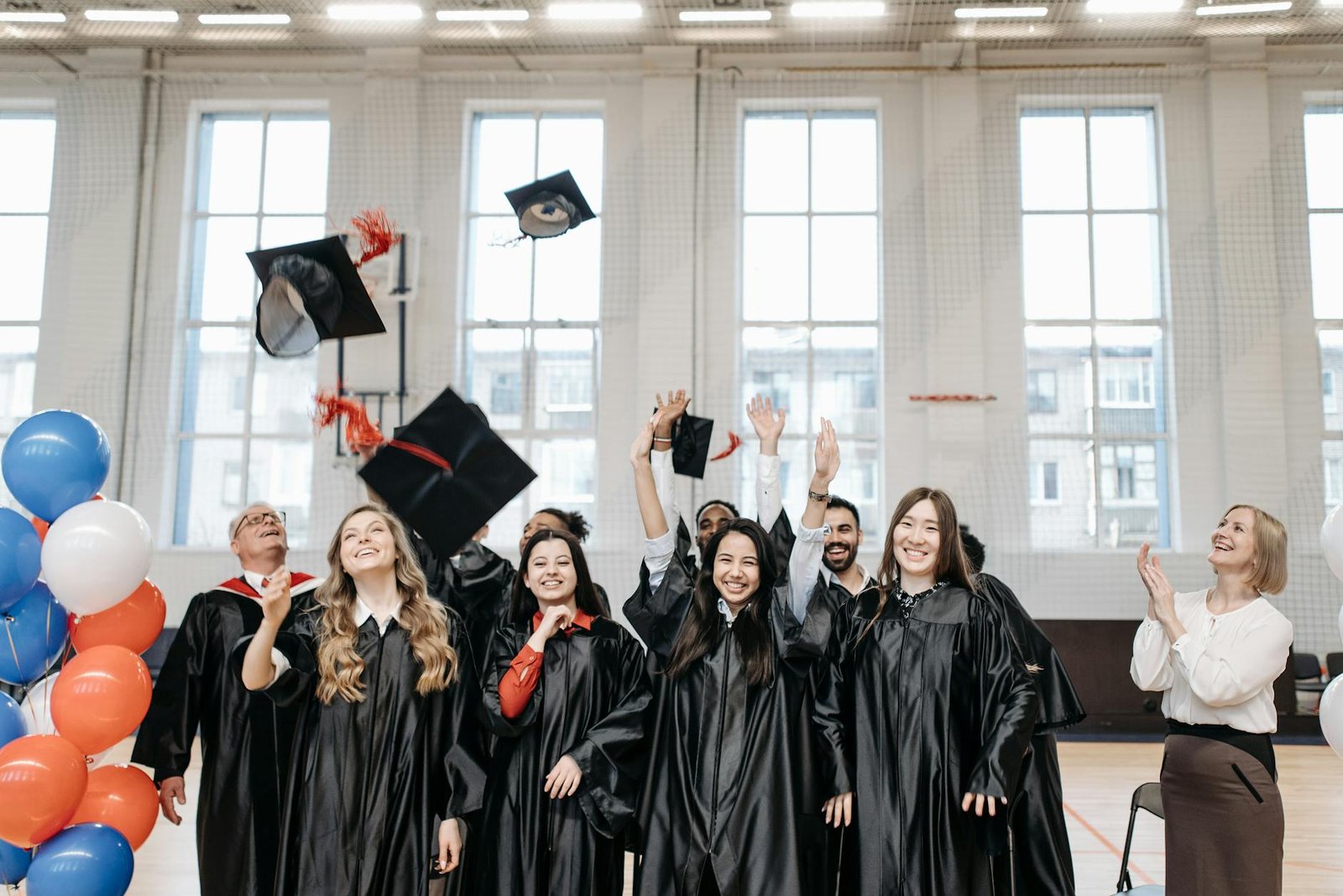 Graduates celebrate by tossing caps in a sports hall, symbolizing success and accomplishment.