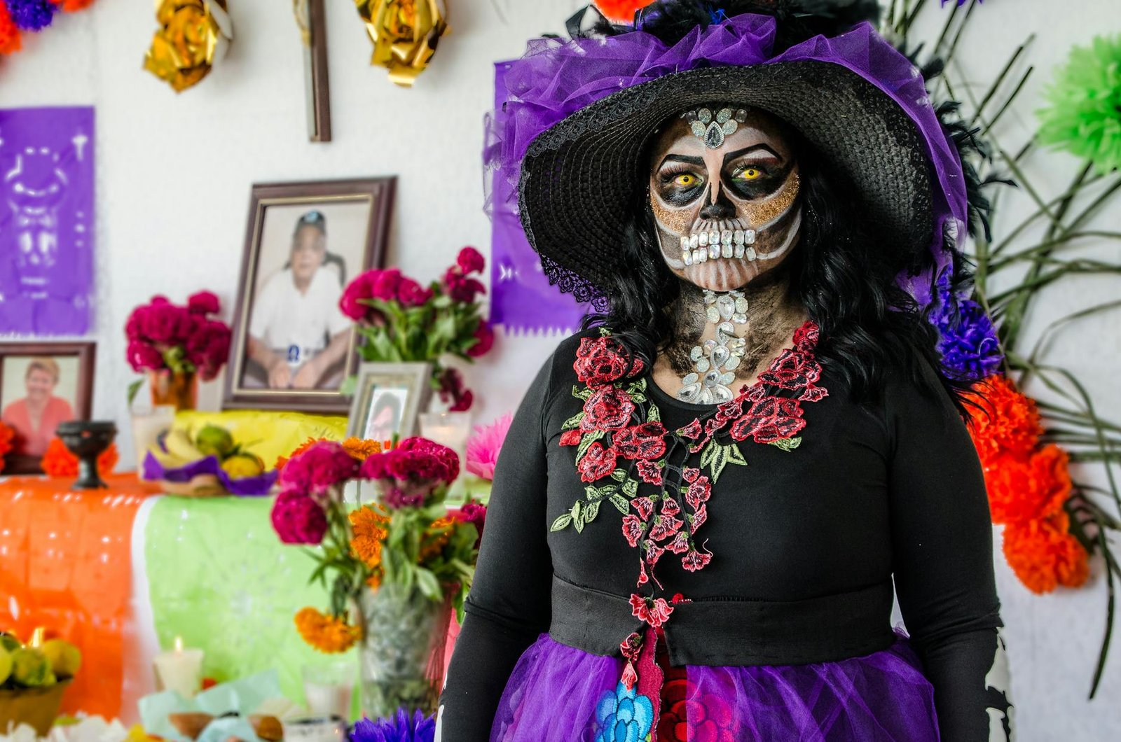 Colorful portrait of a woman in Day of the Dead costume with altar in background.