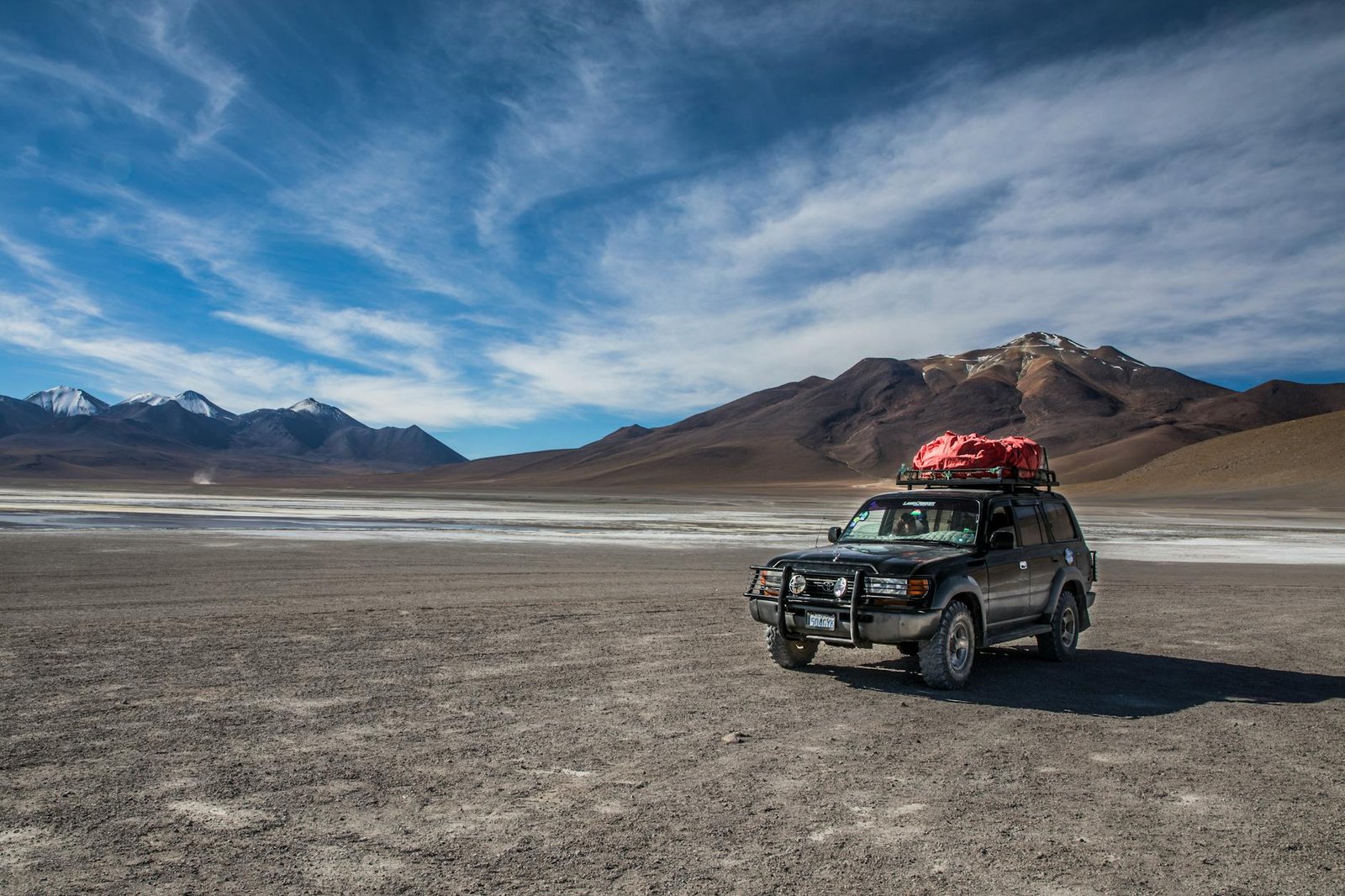 A rugged SUV parked in the expansive desert landscape of Bolivia's Altiplano with a vivid blue sky and distant mountains.