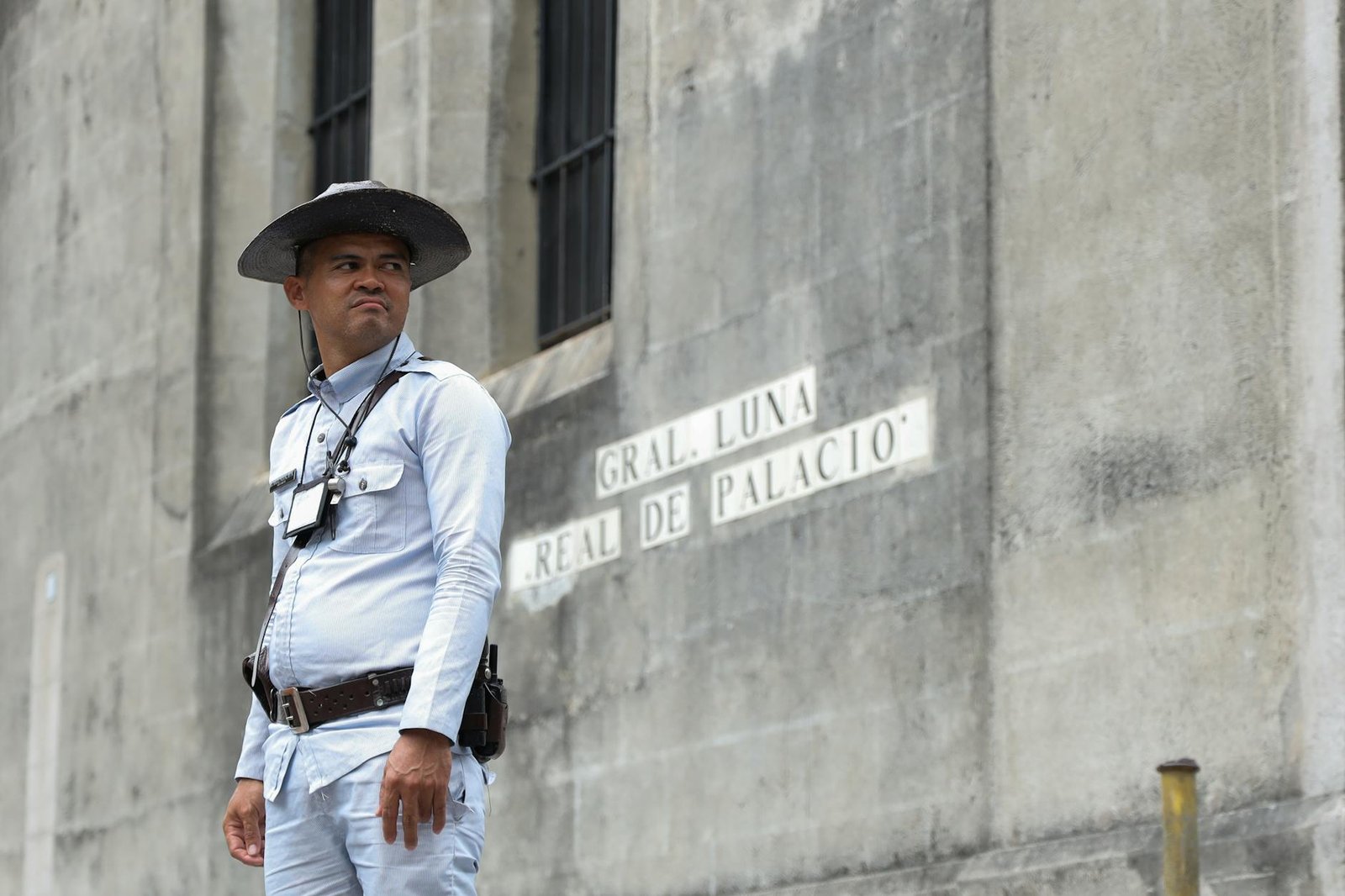 A guard in uniform stands by a historic building in Manila. Street sign reads 'Gral. Luna Real De Palacio'.