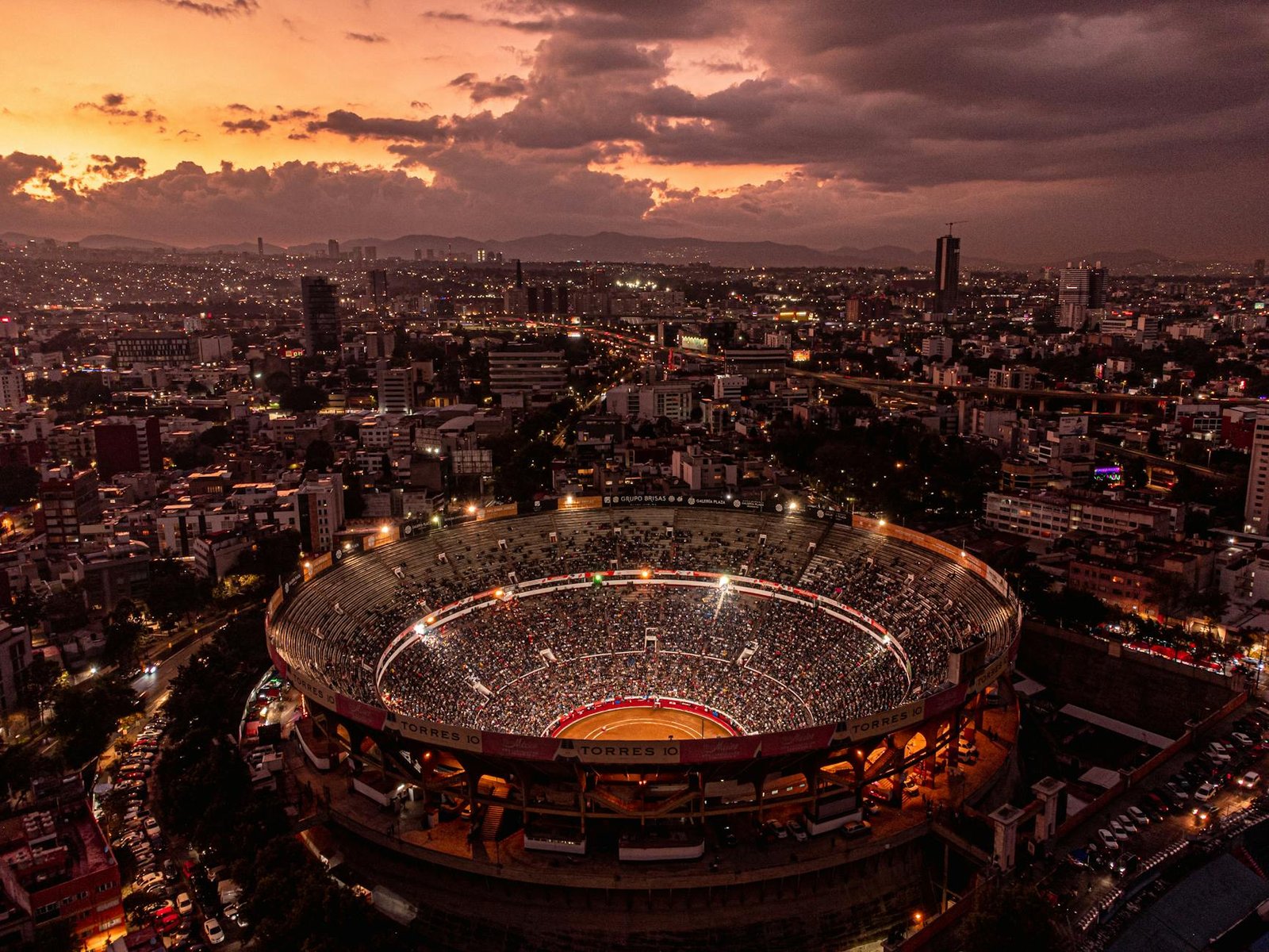 Stunning aerial shot of Mexico City's bullring and skyline at sunset, capturing vibrant urban life.