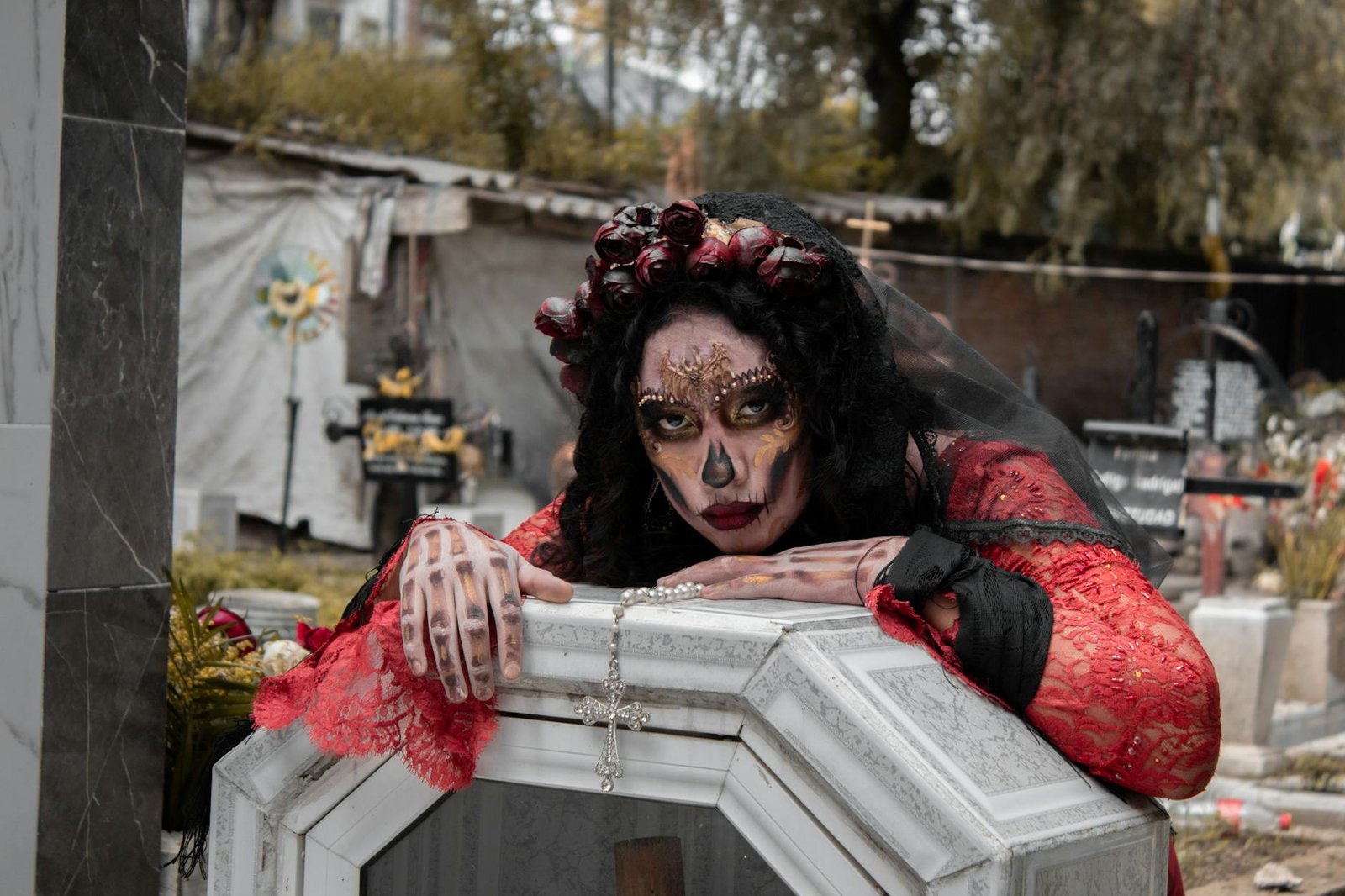 A woman in Dia de los Muertos makeup poses in a cemetery with traditional dress.