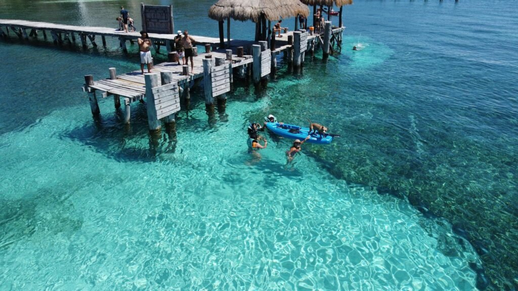 People enjoying a sunny day at Isla Mujeres pier with clear water and vibrant scenery.