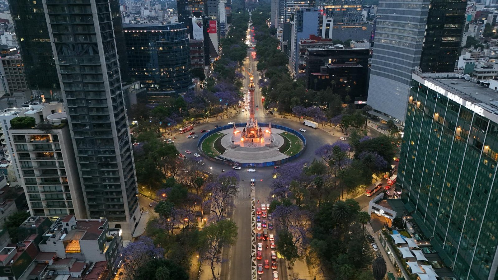 A stunning aerial view of Paseo de la Reforma in Mexico City, vibrant with city lights and jacaranda trees in bloom.