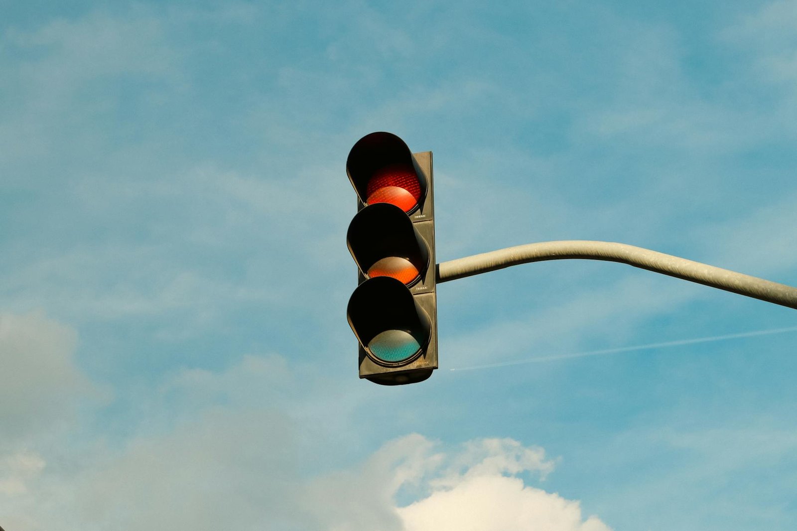 A traffic light with red signal set against a blue sky, signifying stop in urban streets.