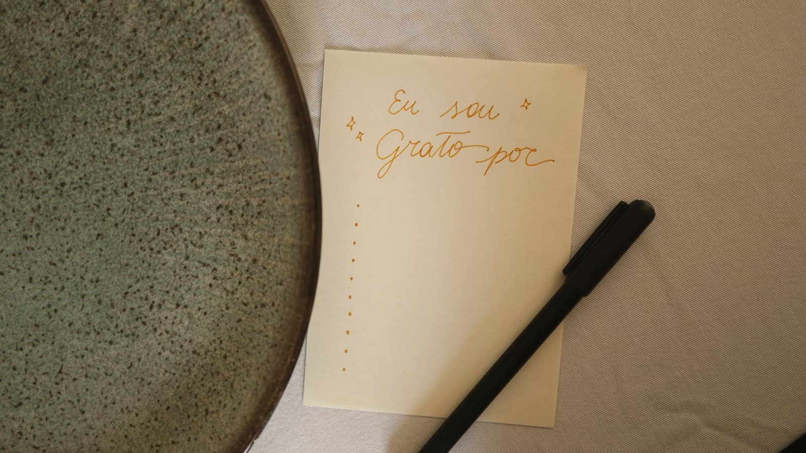 A note in Portuguese showing gratitude, accompanied by a pen and plate, on a table.