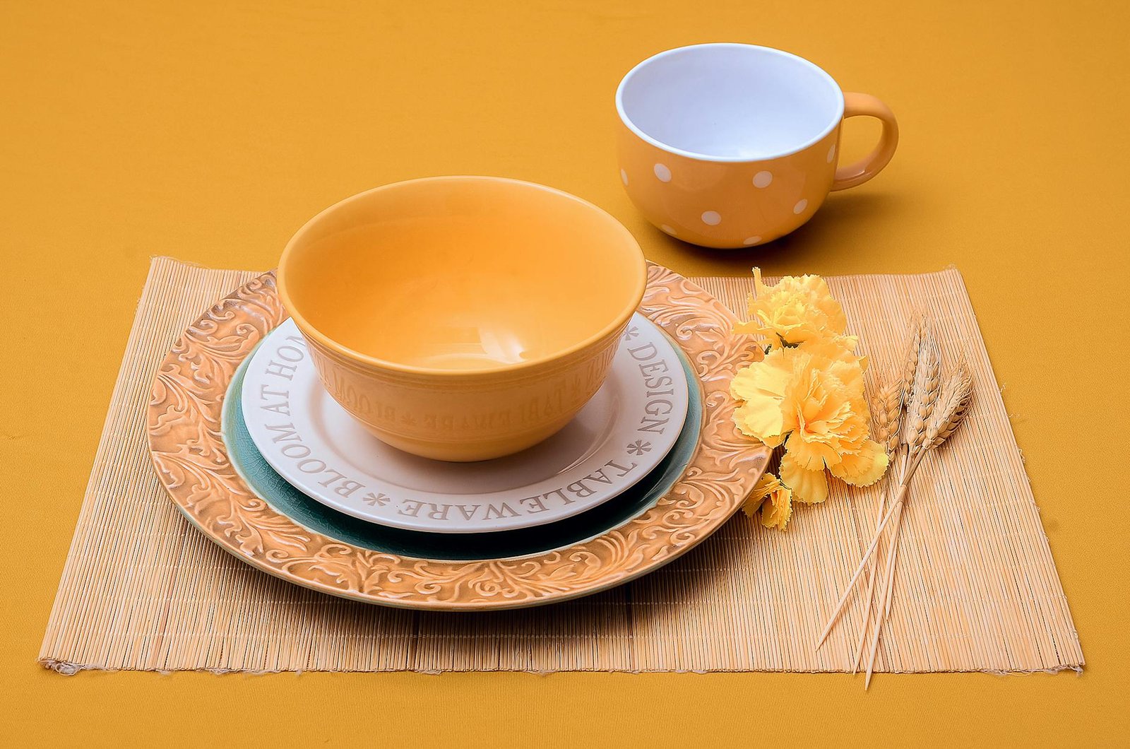 Elegant yellow ceramic dishes on a bamboo mat with flowers and wheat accents.