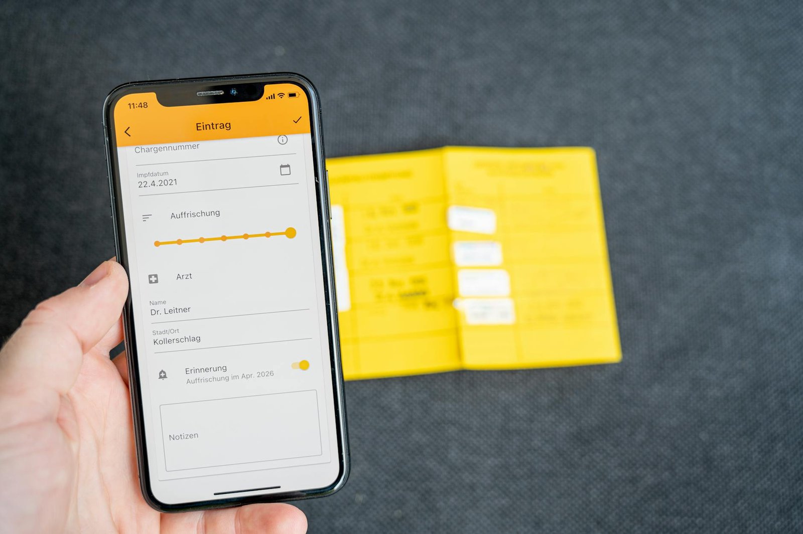 Close-up of a smartphone displaying a health record app held in hand with vaccine card visible.