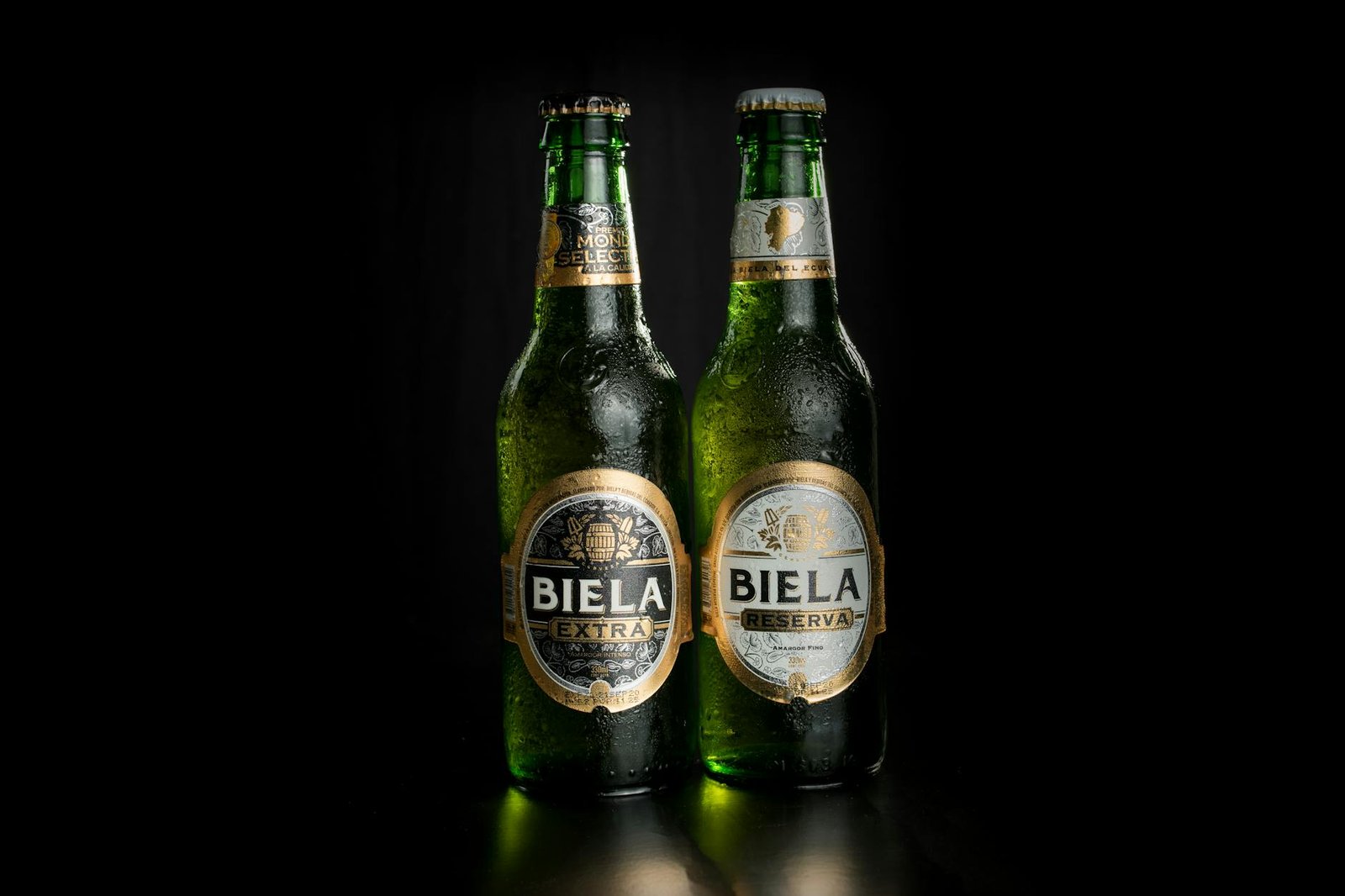 Refreshing Biela Extra and Reserva beer bottles with water droplets on a black backdrop.