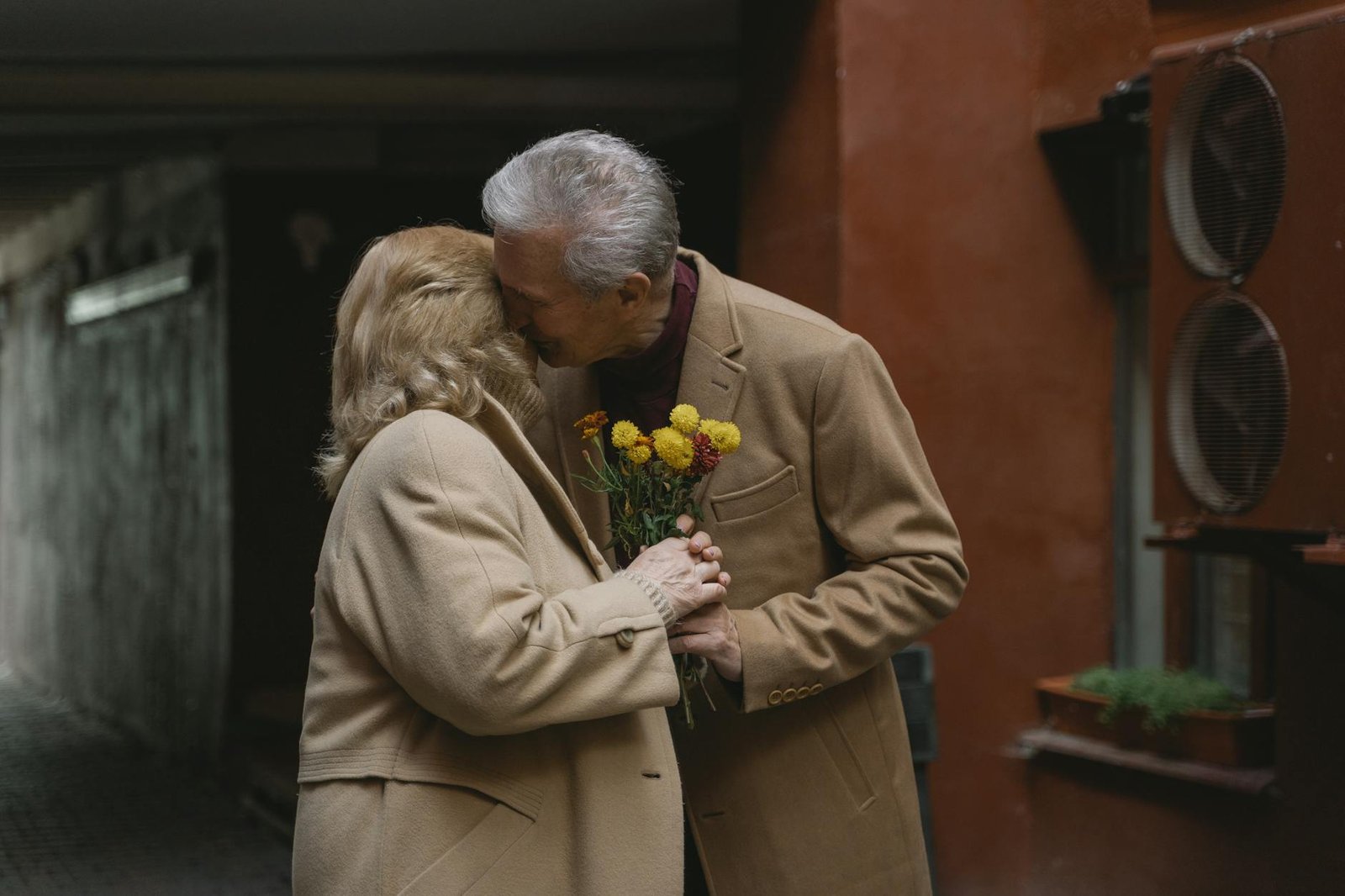 Senior couple sharing a tender moment with flowers in an outdoor courtyard.