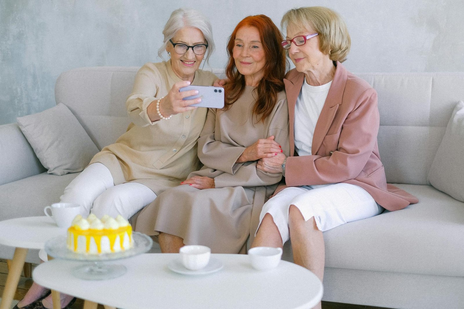Happy senior women taking selfie on mobile phone at table with sweet delicious cake and cups