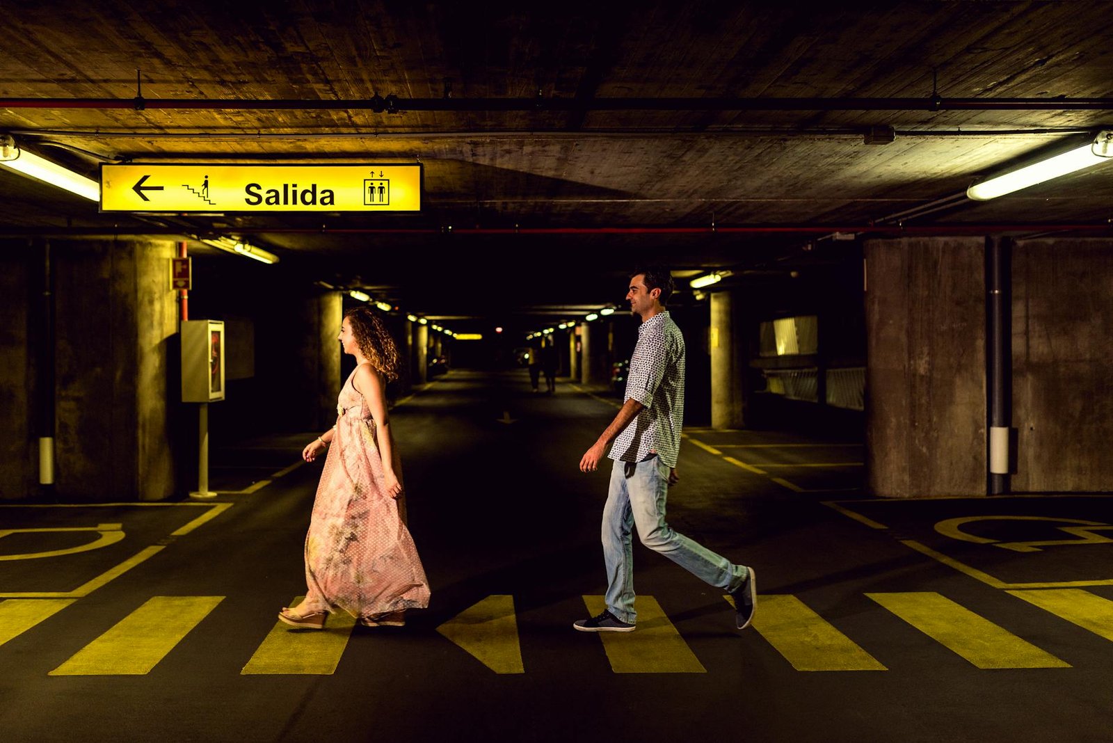 A couple strolling in a dimly lit underground parking garage in Toledo, Spain.