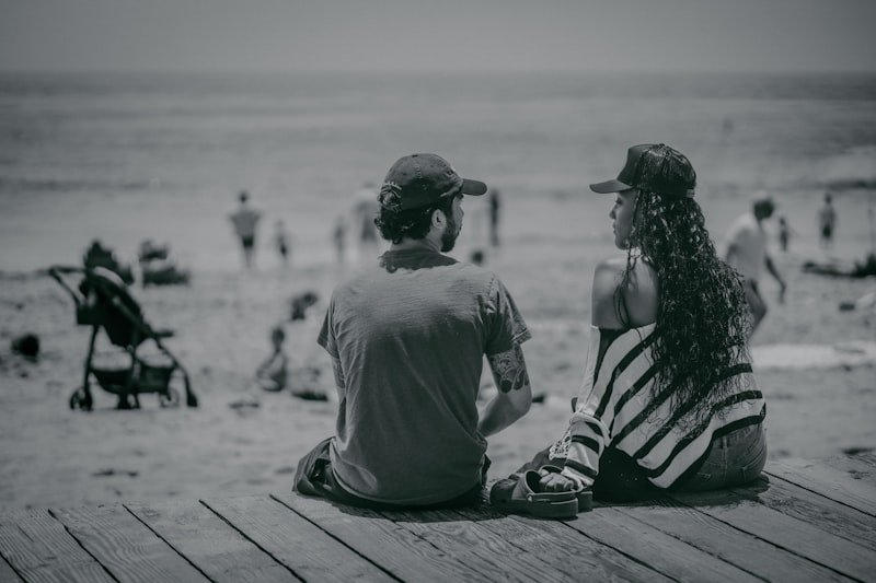 a man and a woman sitting on a pier looking at the beach