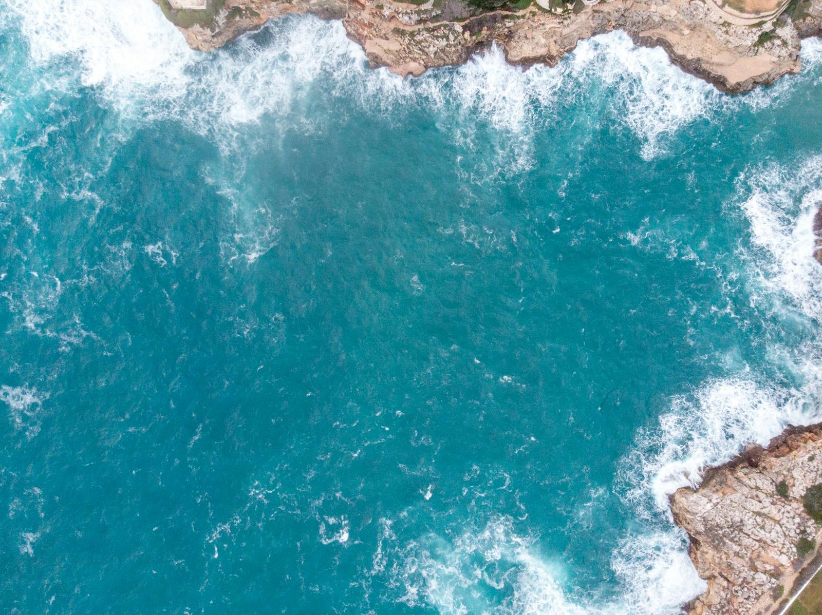Drone shot capturing the vibrant blue waters and rocky coastline of Menorca, Spain.