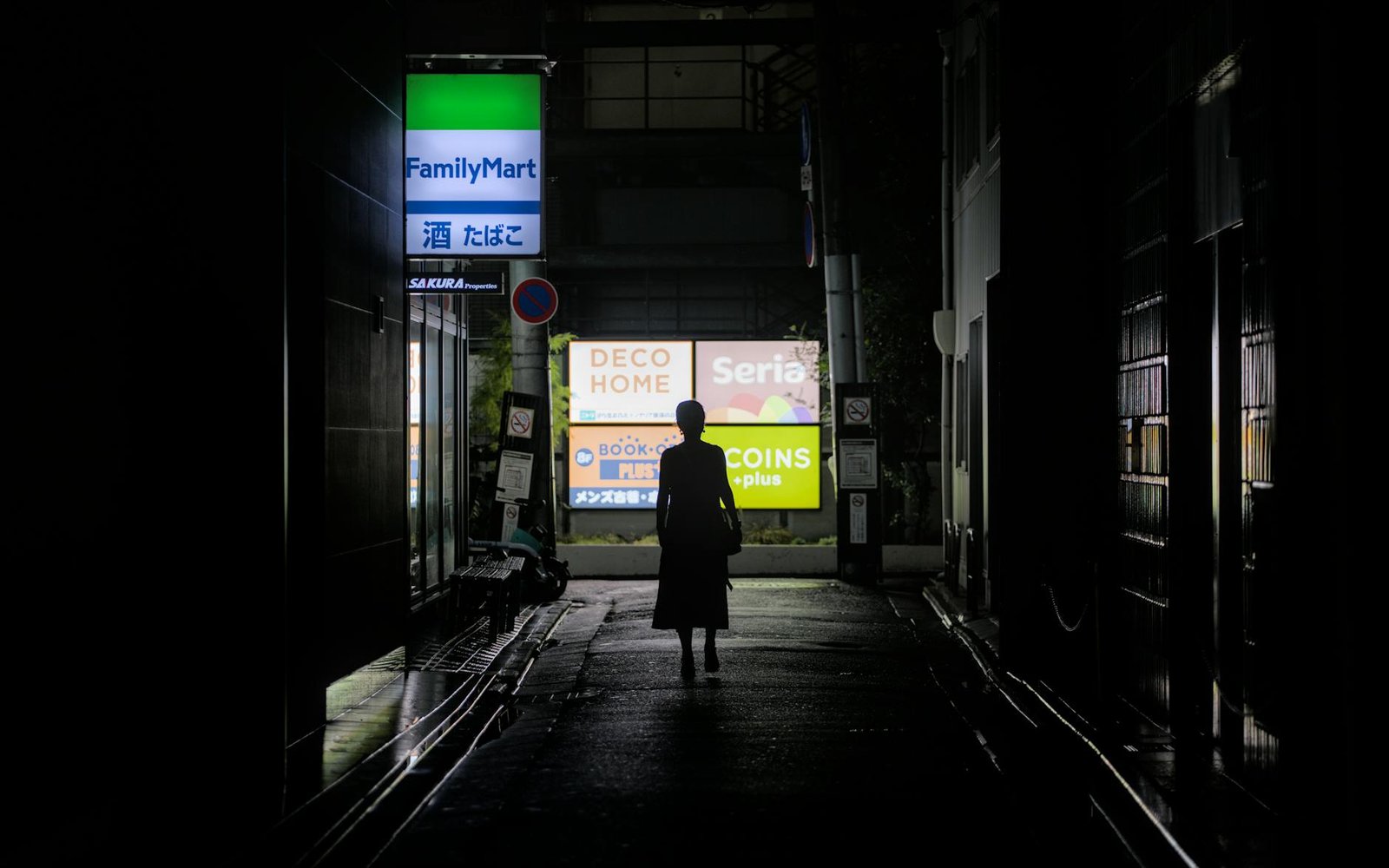 Silhouette in a Kyoto alley at night with urban signage lighting the path.
