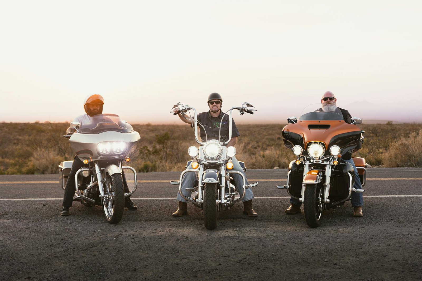 Three bikers on motorcycles riding on a scenic road during sunset in New Mexico.