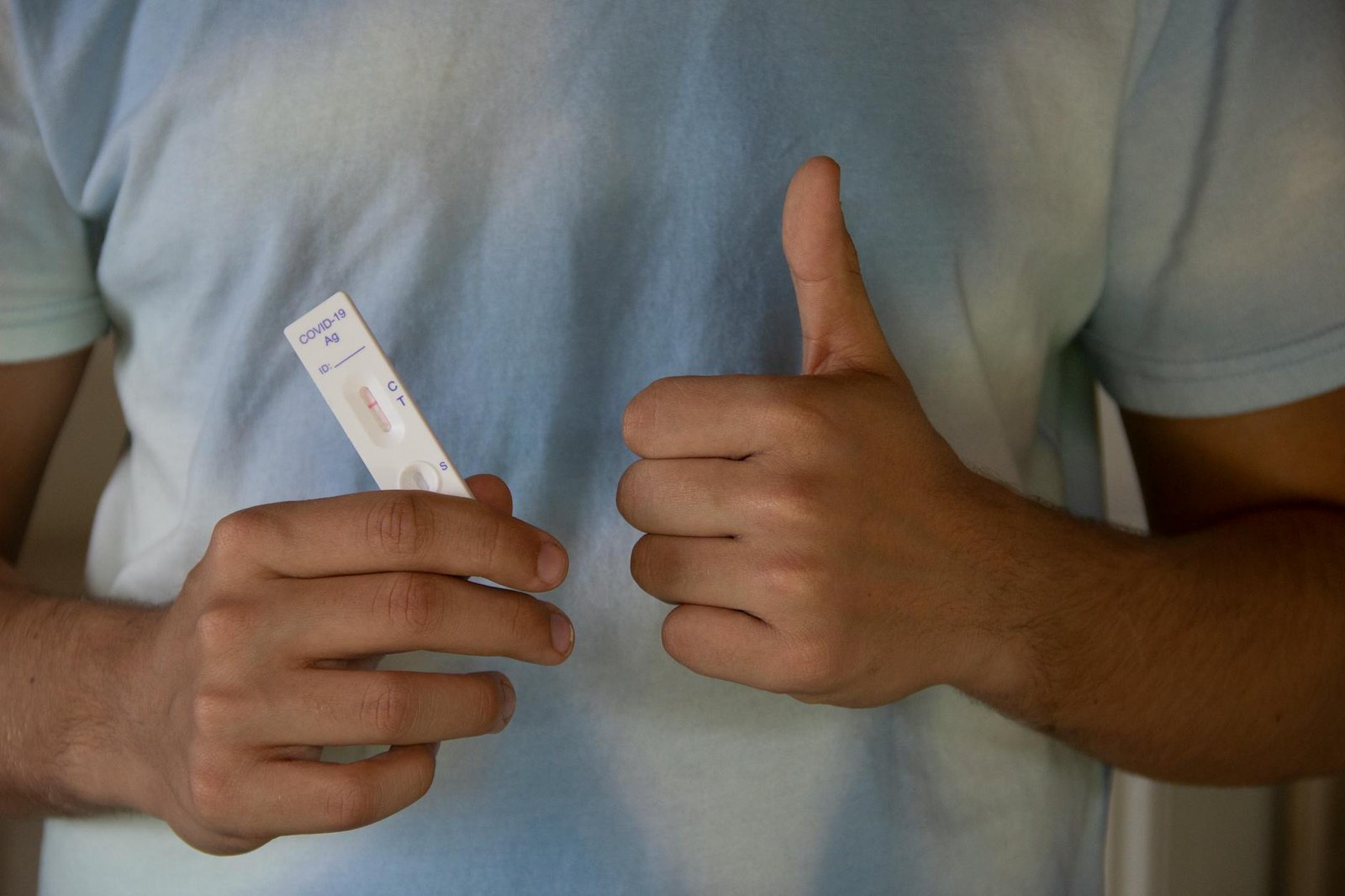 A person showing a COVID-19 antigen test and giving a thumbs up, indicating a negative result.