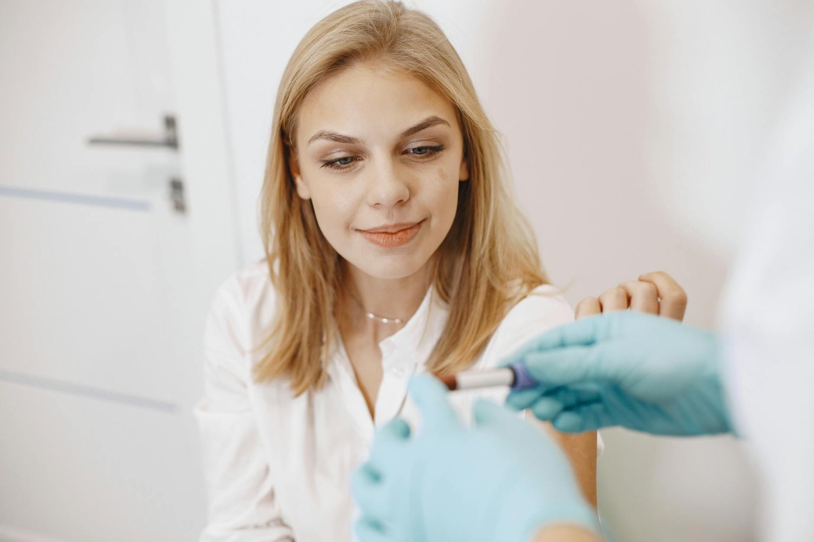 Blond woman in clinic receiving blood test with healthcare professional holding sample.
