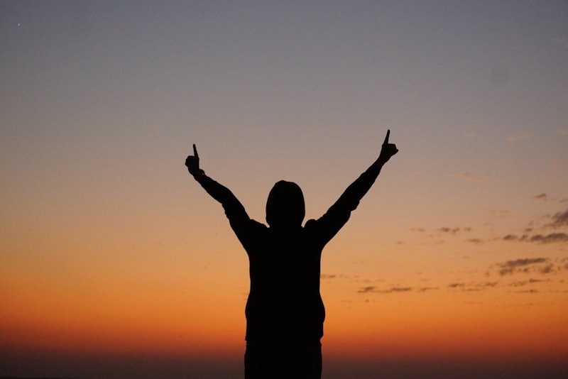 a person with their arms in the air at sunset