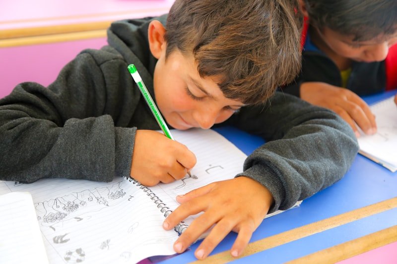 Two young boys sitting at a desk writing on paper