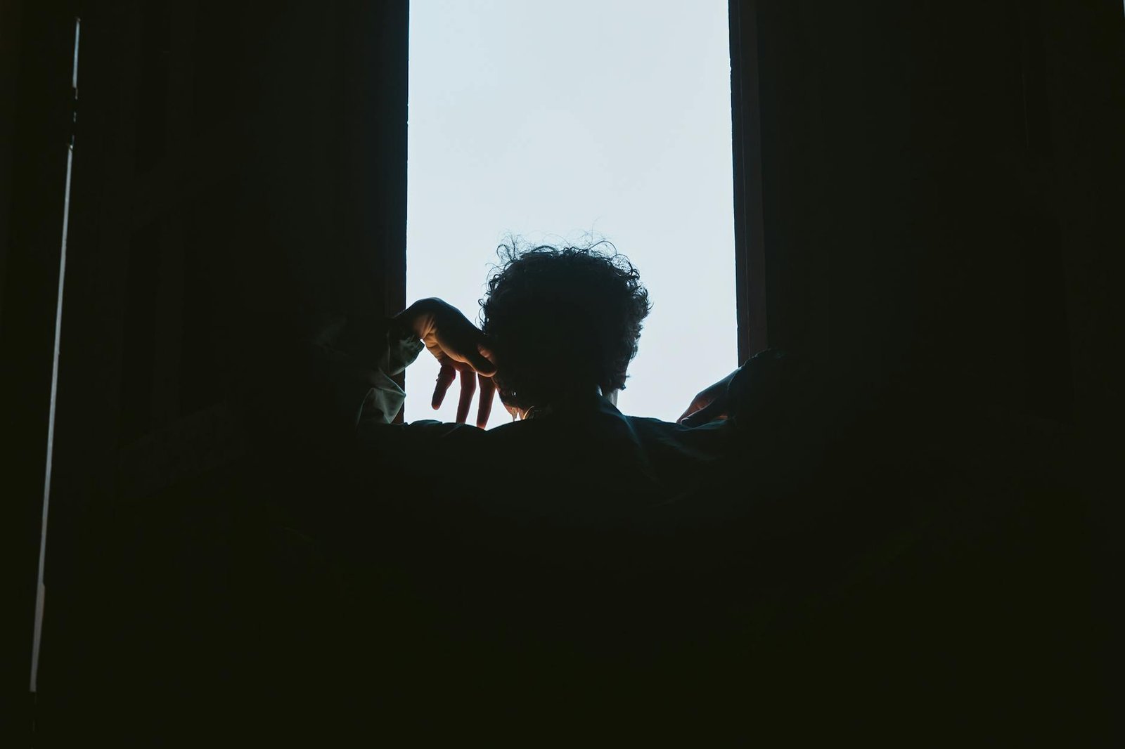 A person silhouetted against a bright window, creating a dramatic contrast between light and shadow.